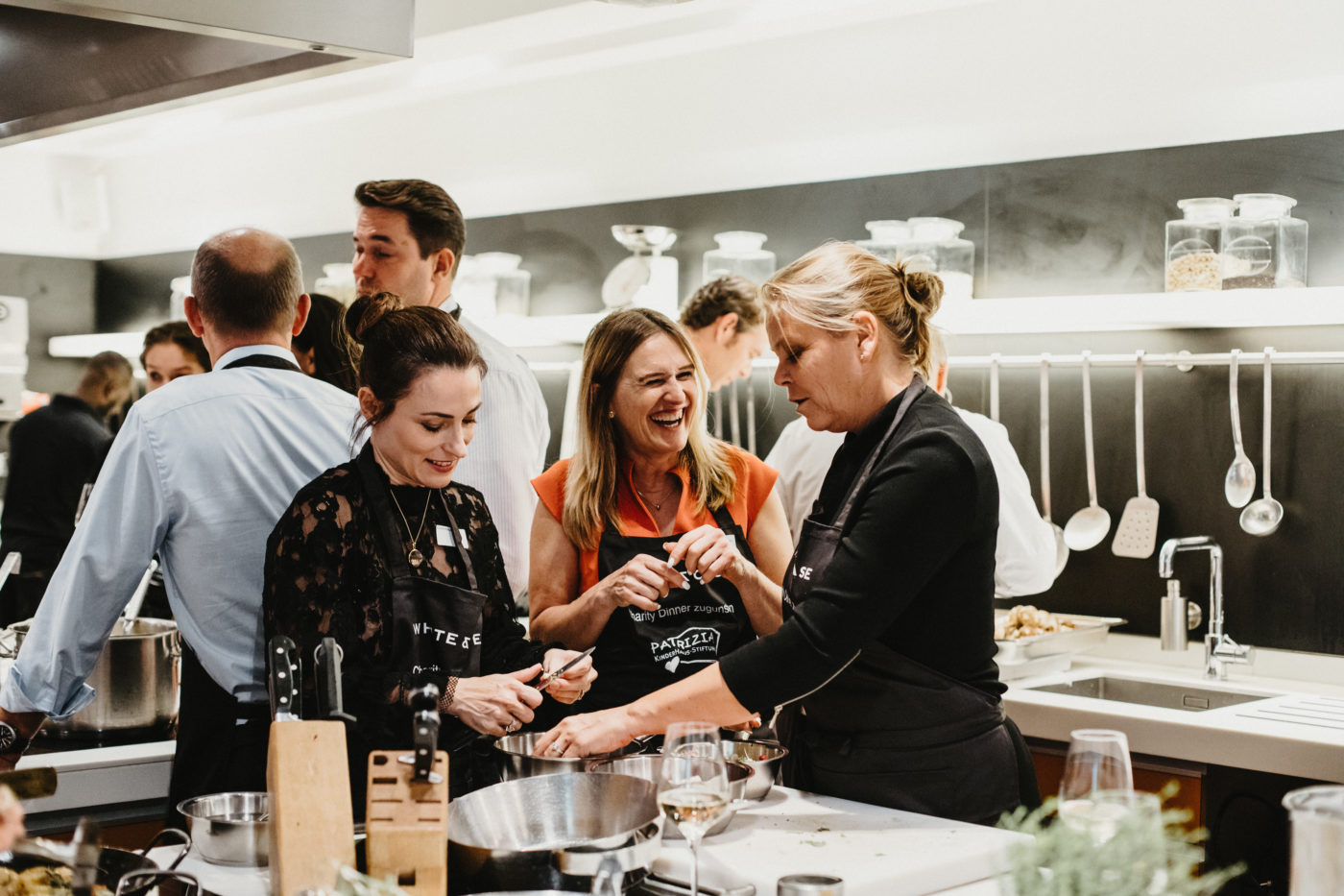 Event PATRIZIA Charity Cooking 2018 Frankfurt mit White & Case LLP, Gäste lachen mit Schürze